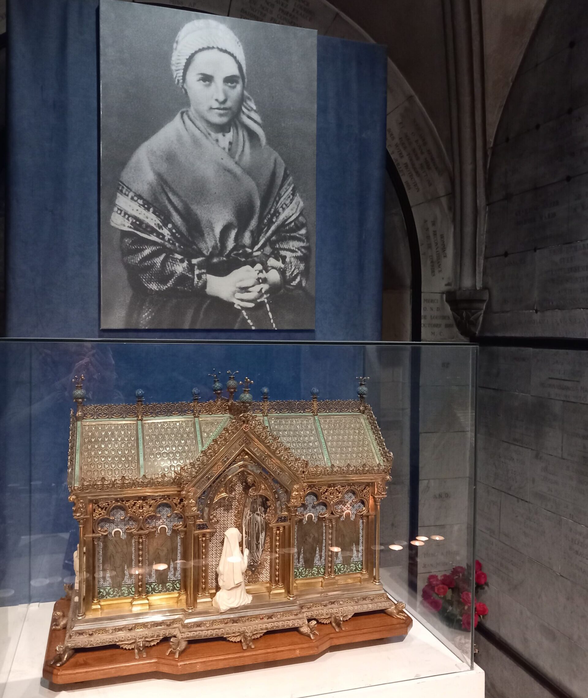 Egy fiatal nő fekete-fehér fényképe a falon, előtte díszes ereklyetartó