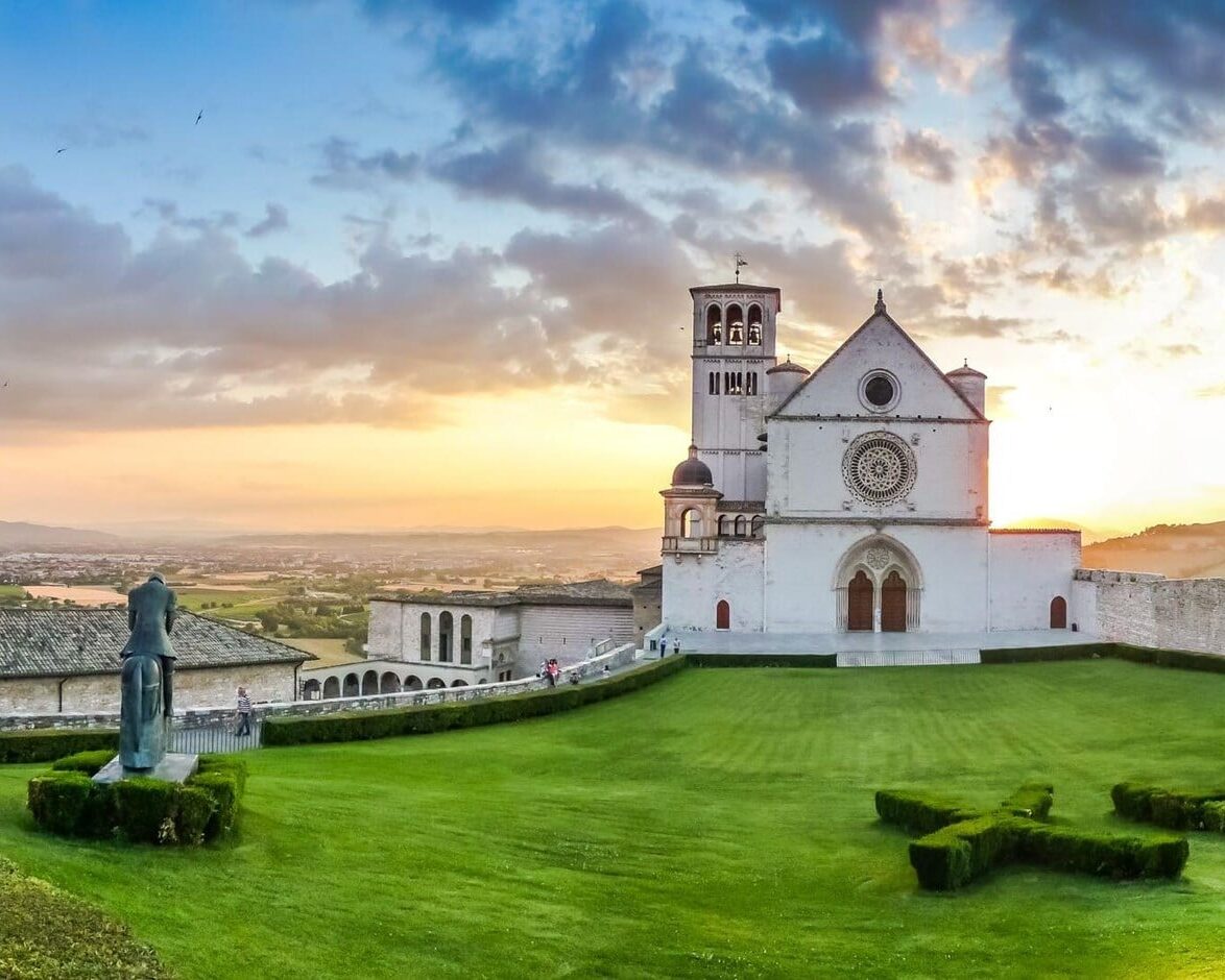 Egy nagy középkori templom rózsaablakkal, előtte zöld terület egy lovasszoborral, a háttérben egy völgy